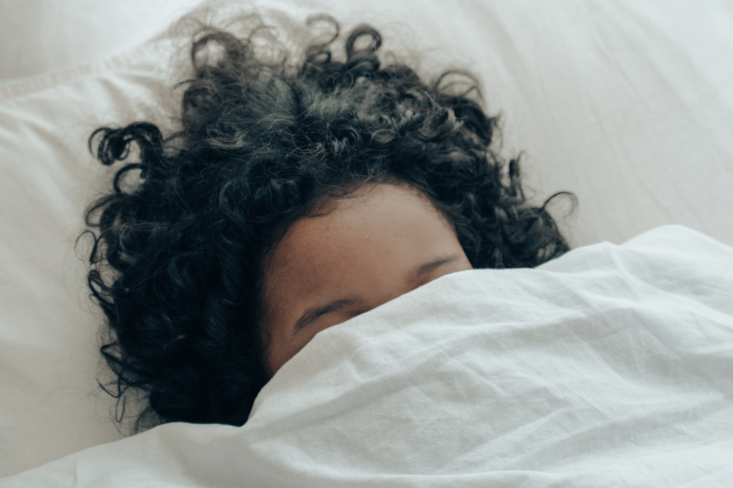 person lying down in bed with blanket pulled 